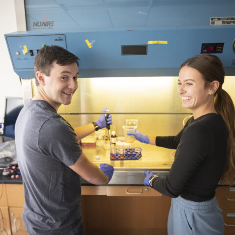 A young male and female laughing together in front of a hood vent while working on a science project.