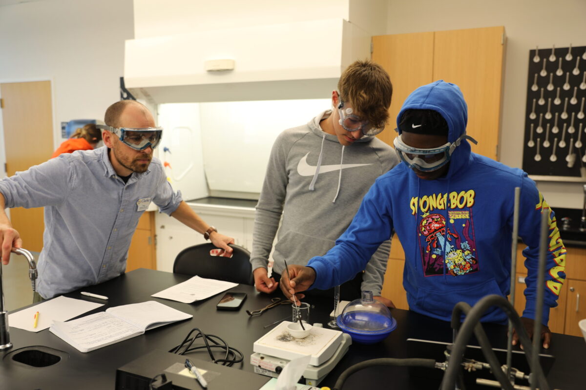 A male teacher watching over two male's chemistry experiment. - Full Size