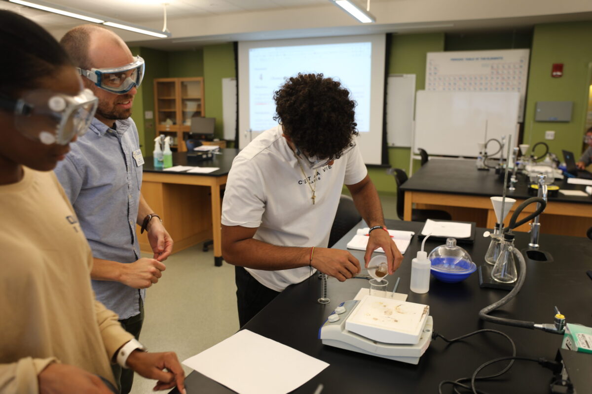 A male teacher watching a student measure ingredients. - Full Size
