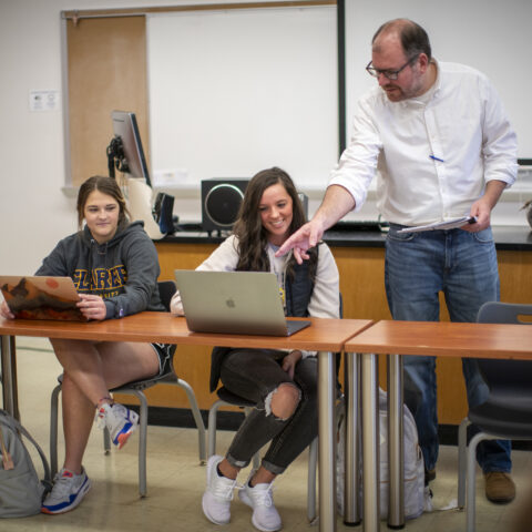 A male teacher standing over a student discussing the work on her laptop.