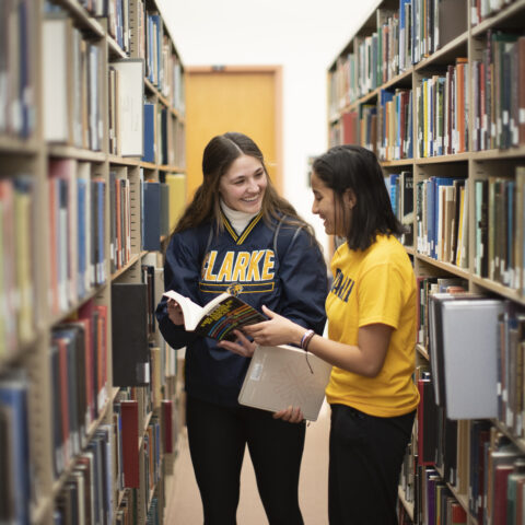 Two female students discussing the contents of a book in a library.