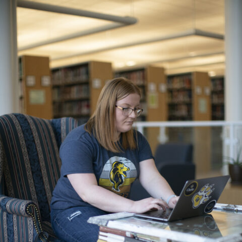 A female student studying on her laptop next to a pile of books.