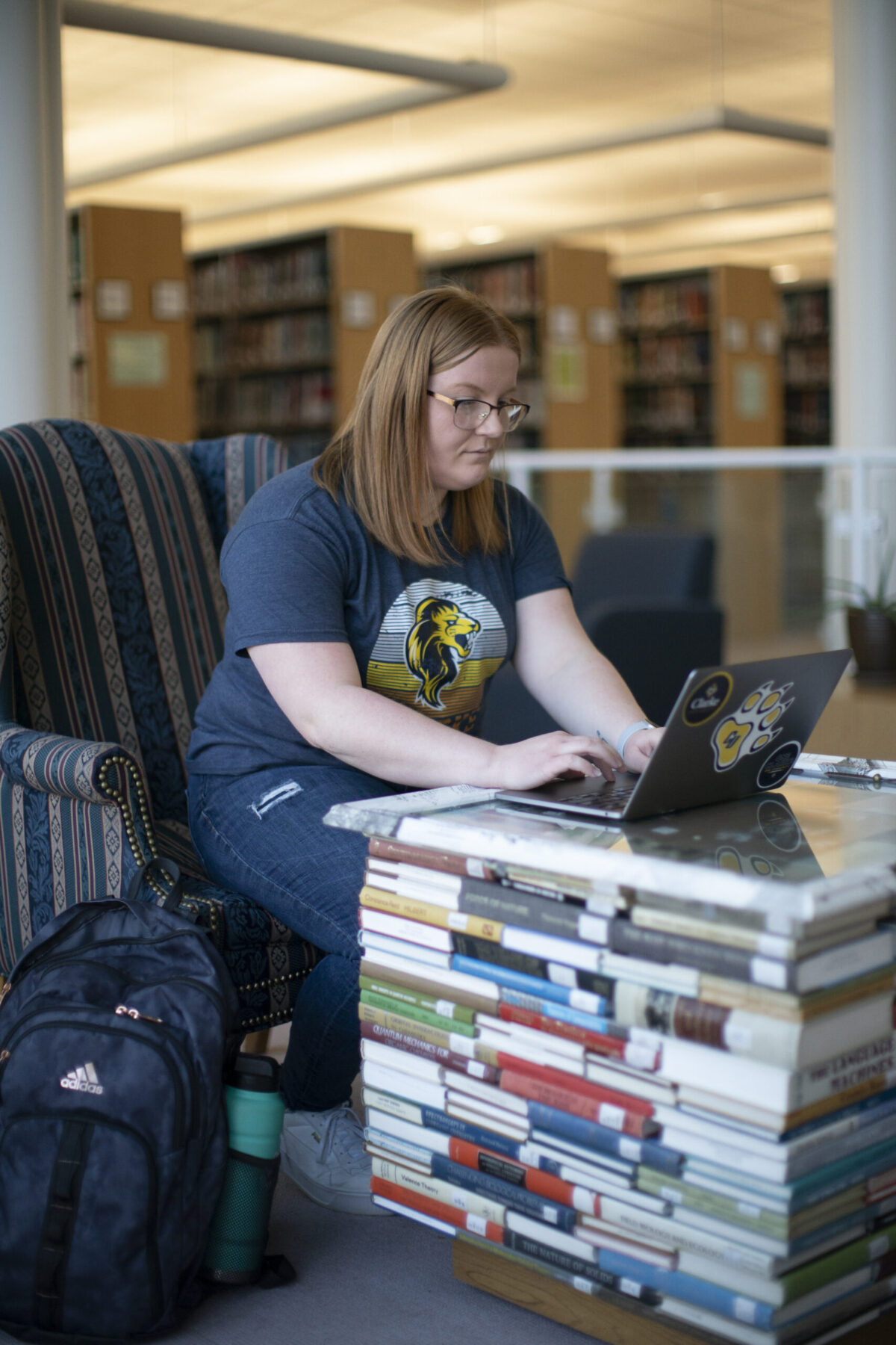 A female student studying on her laptop next to a pile of books. - Full Size