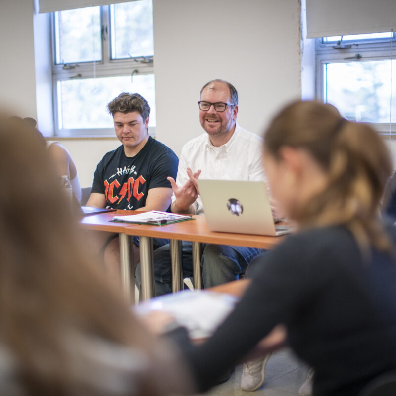 A male teacher sitting next to his students.