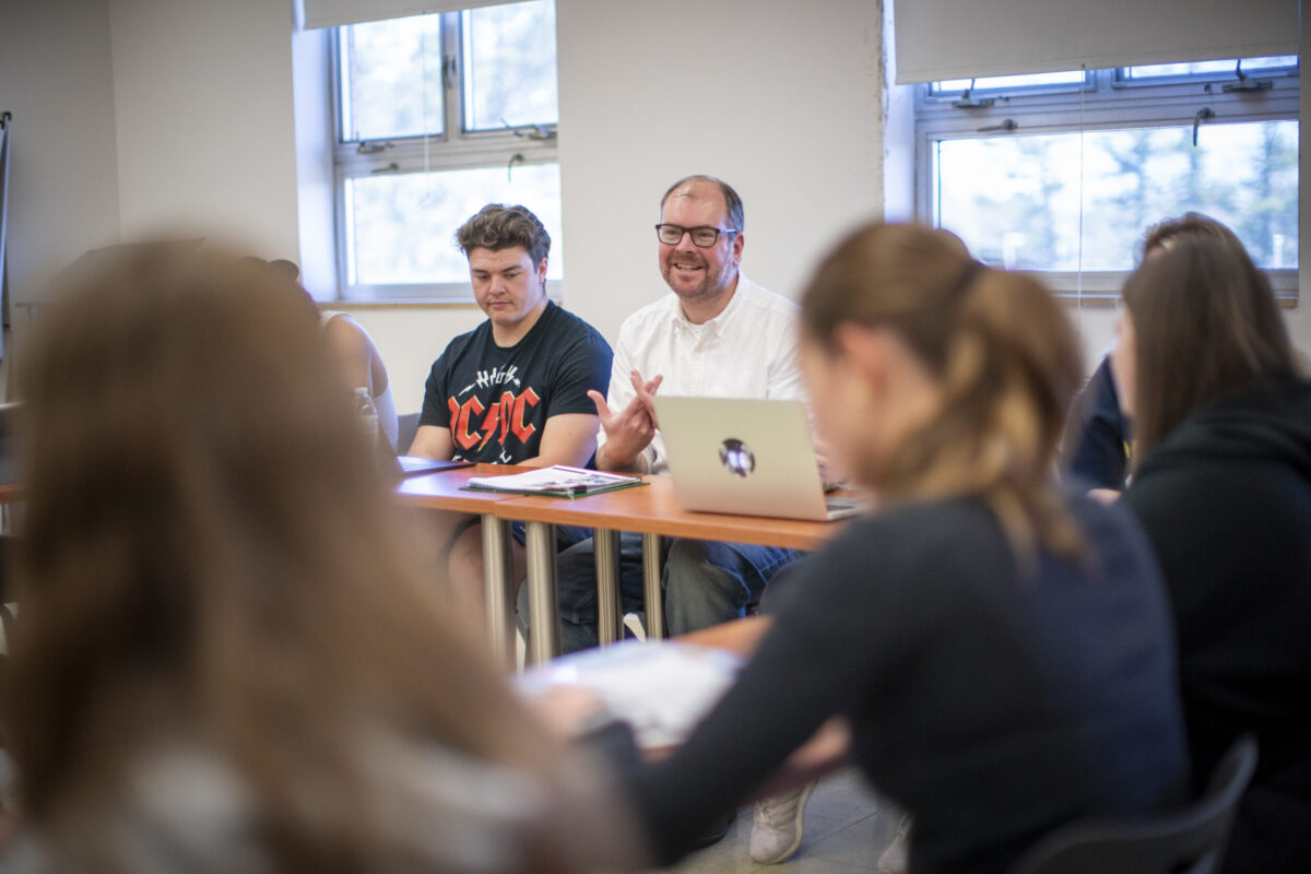 A male teacher sitting next to his students. - Full Size