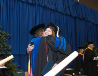 A graduate hugging her professor after receiving diploma.