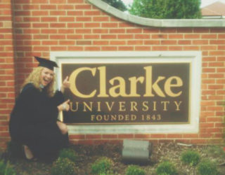 Graduate in front of the Clarke University Campus sign.