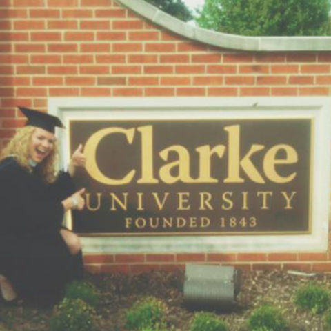 Graduate in front of the Clarke University Campus sign.